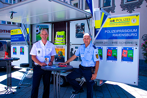 Zwei Beamte des Referats Prävention vor dem mobilen Informationsstand des Polizeipräsidiums Ravensburg.